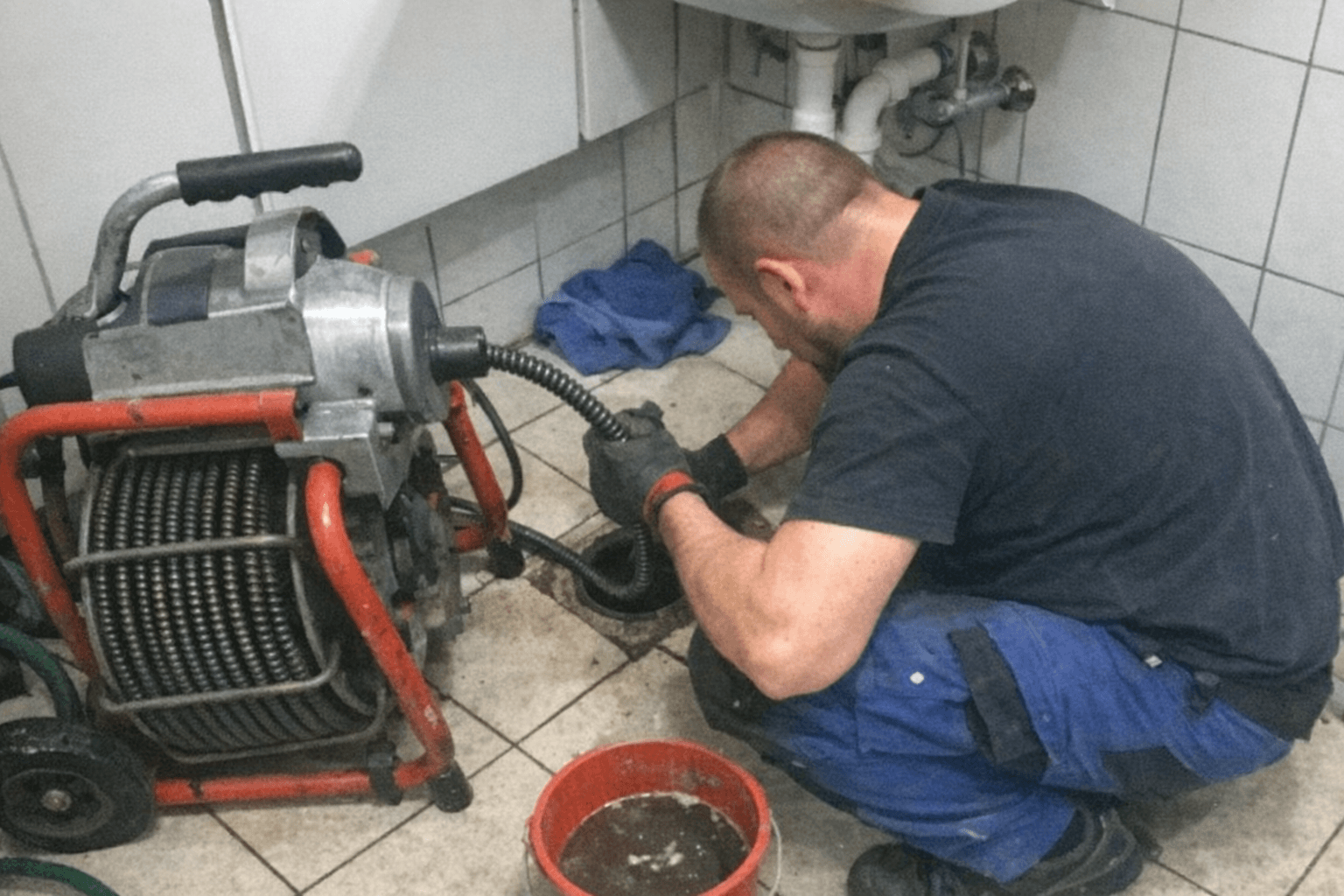 Fachmonteur führt eine Motorspirale in ein geöffnetes Revisionsrohr im Keller ein